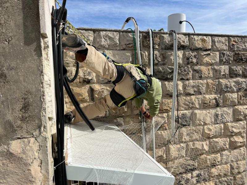 איש מקצוע מתקין רשת להרחקת יונים בגובה